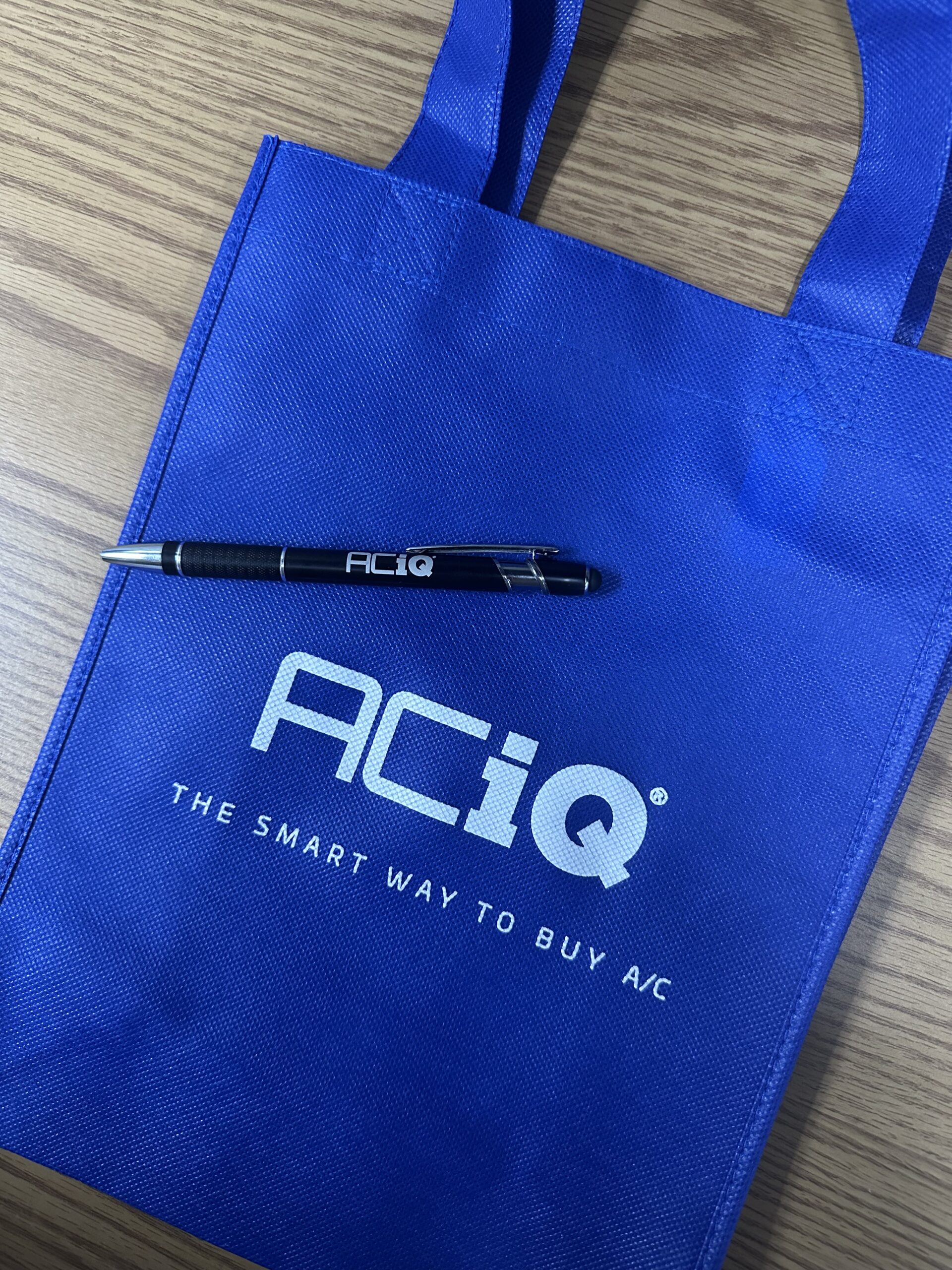 ACiQ branded tote bag and pen on wooden table – HVAC marketing giveaway for ACiQ dealers