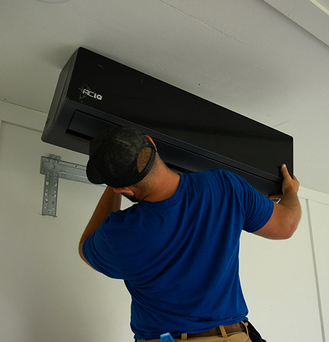 Technician installing an ACiQ wall-mounted air handler for a ductless mini split system inside a home