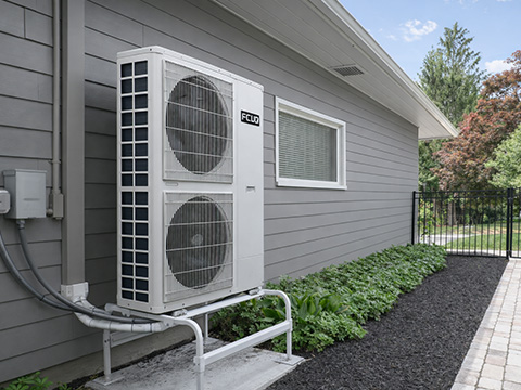 ACIQ Essentials R32 heat pump outdoor condenser installed beside residential home exterior