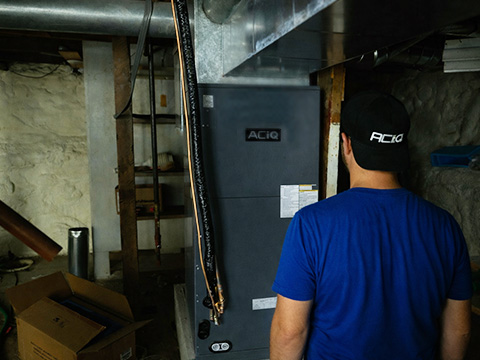 Technician standing near installed ACIQ Essentials central heat pump air handler in basement mechanical room