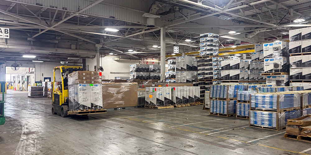 Forklift moving palletized ACiQ equipment through a stocked HVAC warehouse.