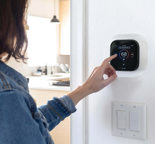 Homeowner adjusting a smart thermostat to improve HVAC efficiency and manage rising electrical costs