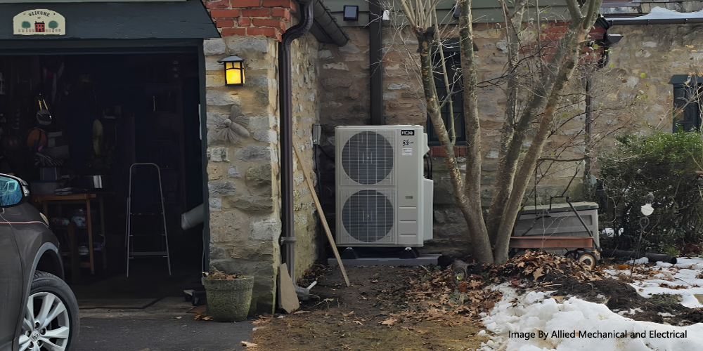 ACiQ multi-zone mini split outdoor unit installed beside a stone home in winter