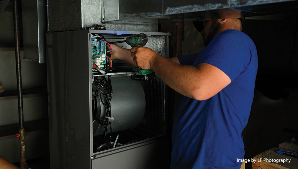 HVAC technician using a power drill while working on internal components of an indoor heating and cooling system